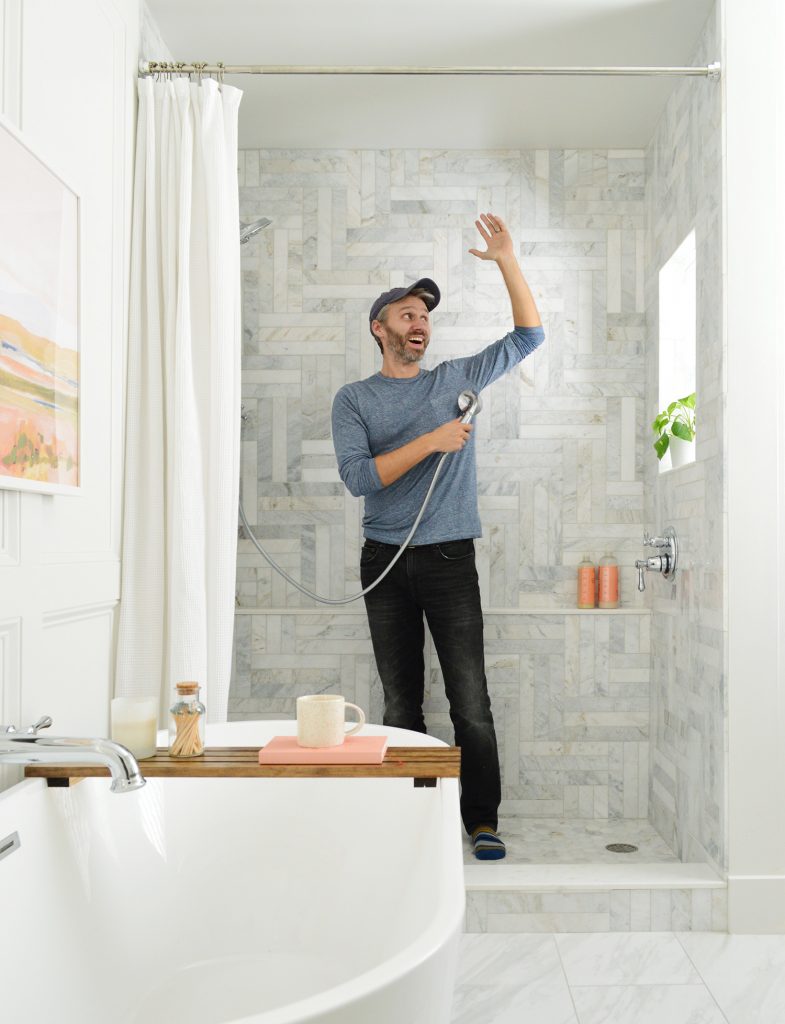 John standing in marble tiled shower pretending to shower