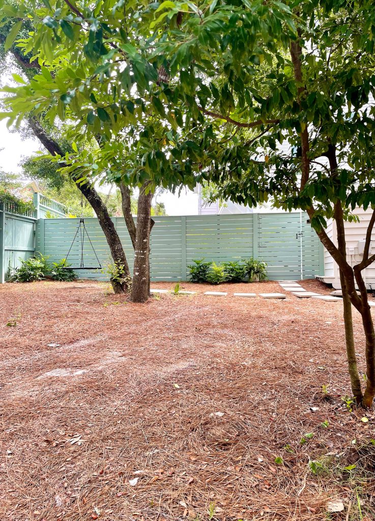 View of gray green horizontal pool fence from outside with live oak tree in foreground